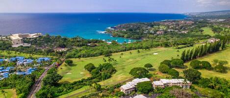 An aerial view of a coastal resort with a golf course, beachfront properties, and a clear view of the ocean.