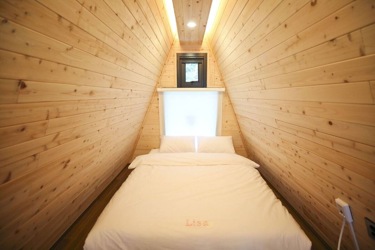 Una habitación estrecha con paneles de madera, una cama, un ventanal pequeño y una lámpara en el techo.