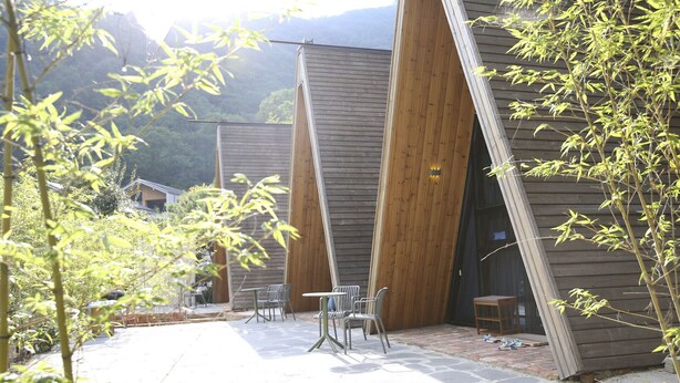 Un edificio con un diseño arquitectónico único, que destaca por grandes paneles de madera y un patio empedrado con mobiliario exterior.