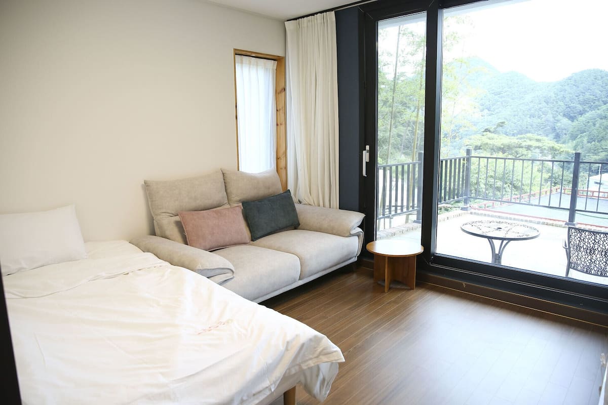 Habitación de hotel con cama, sofá, una mesita y balcón con vistas a zonas verdes.