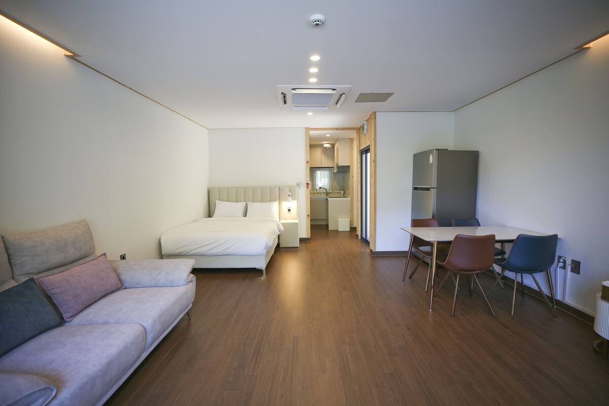 Una habitación de hotel moderna con cama, sofá, mesa de comedor con sillas y kitchenette.