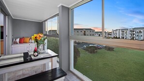 En balkon med udsigt over et boligområde, et bord med en flaske og glas, samt en vase med blomster.