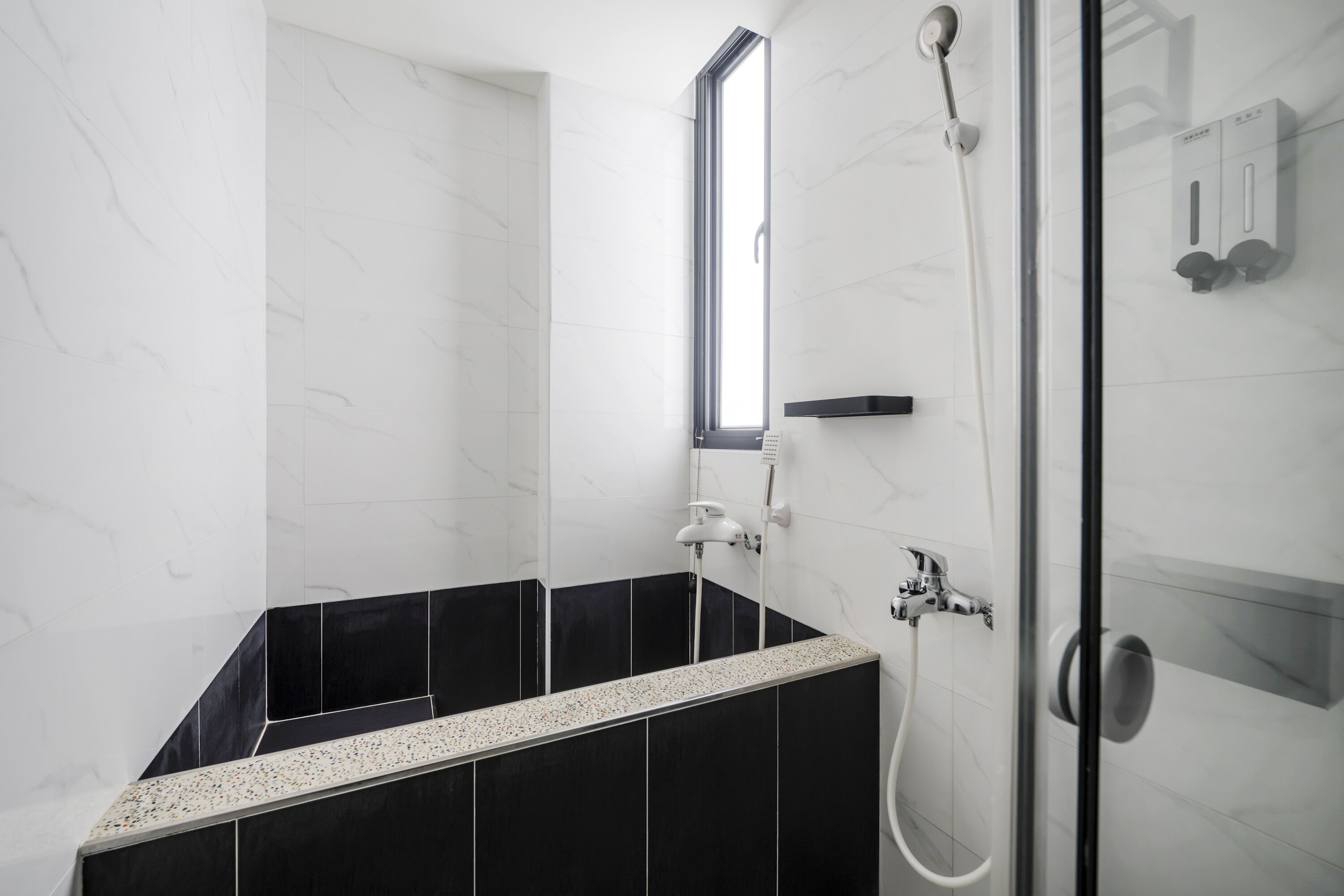 Un baño moderno con cabina de ducha de vidrio, un lavamanos empotrado con encimera de aspecto moteado y un revestimiento de pared de azulejos blanco y negro.
