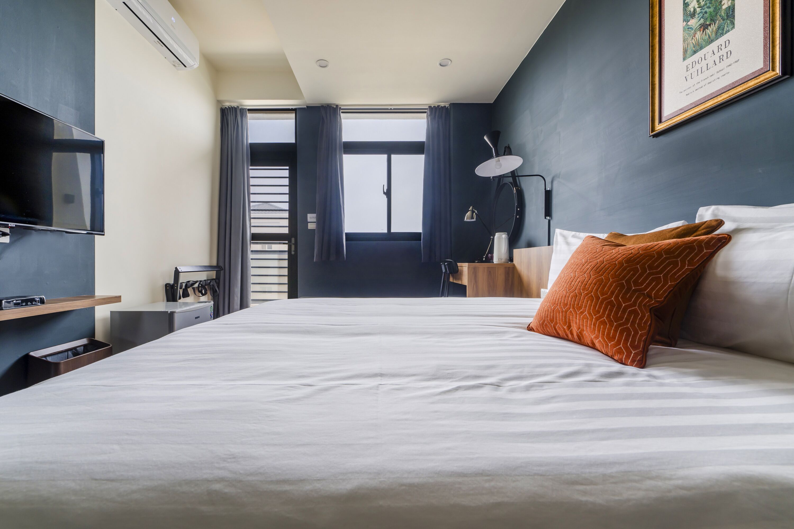 Une chambre d’hôtel avec un lit, une télévision, un bureau et une fenêtre avec des rideaux.