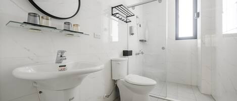 Un baño moderno con lavamanos, inodoro y ducha de mármol blanco.