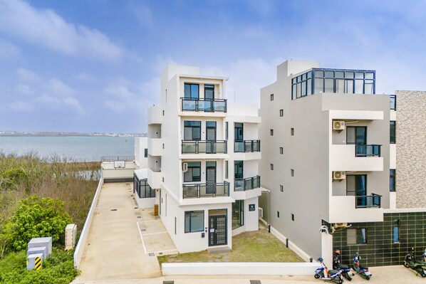 Un immeuble résidentiel moderne à plusieurs étages, doté de balcons, d’un espace de stationnement et offrant une vue sur la mer.