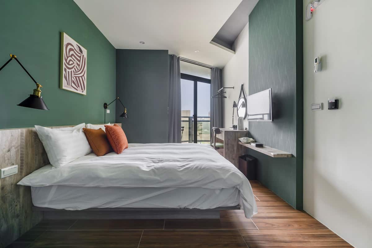 Ein modernes Hotelzimmer mit einem großen Bett, einem Schreibtisch mit Stuhl, einem Flachbildfernseher und einem Balkon mit Aussicht.