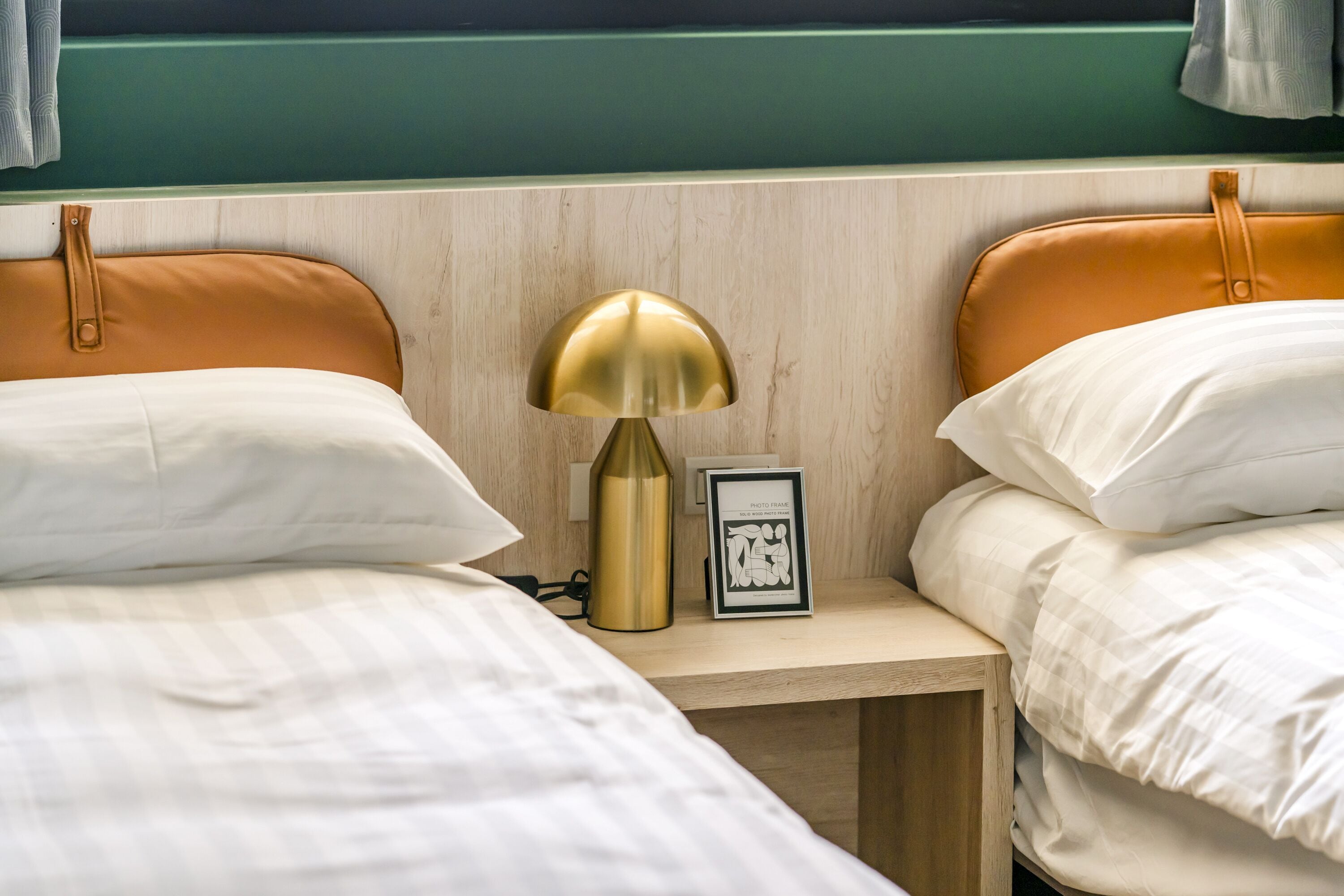 Habitación doble con dos camas, una mesita de noche, una lámpara y un cuadro enmarcado.
