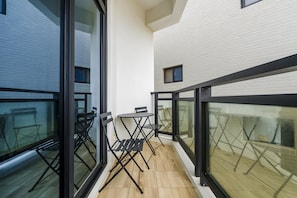 A balcony with a table and chairs, large windows, and a white brick wall.