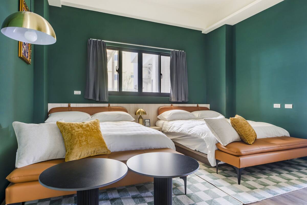 Ein Zimmer mit zwei Betten, einem Vorhangfenster, einem Schachbrettboden und einer Pendelleuchte.