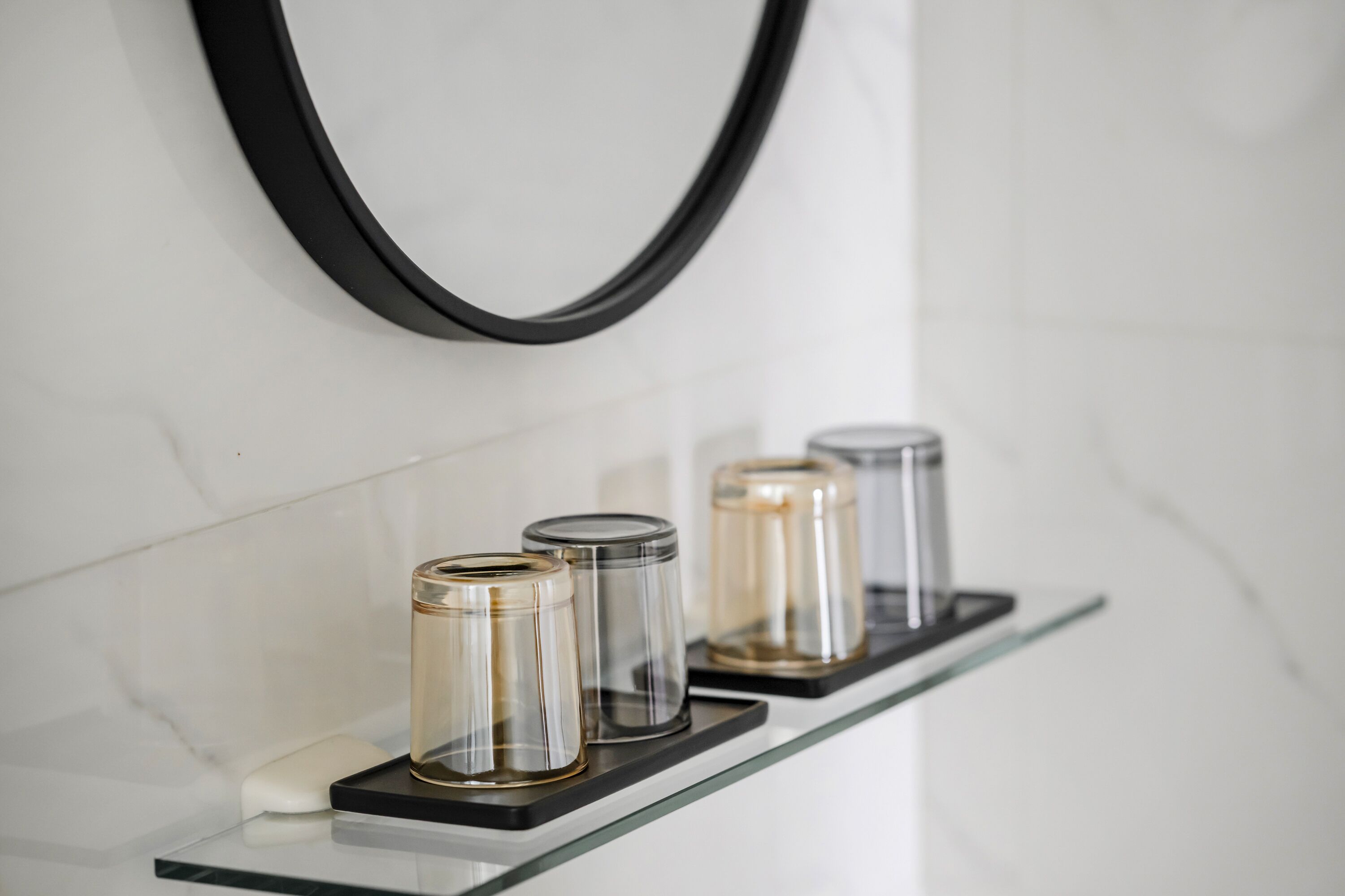 A bathroom with a glass shelf holding three cylindrical containers.