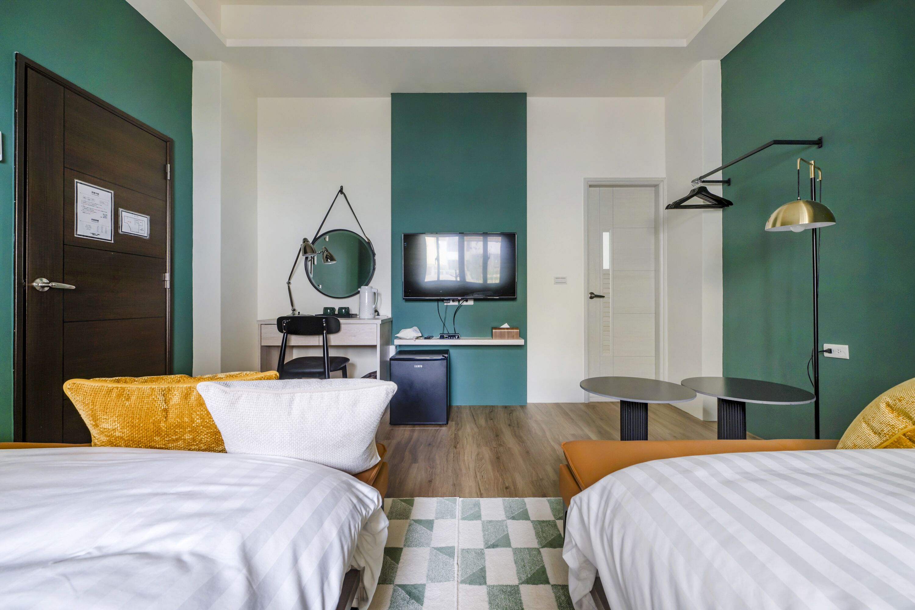 Una habitación de hotel con dos camas, un escritorio con computadora, televisión y un refrigerador pequeño.