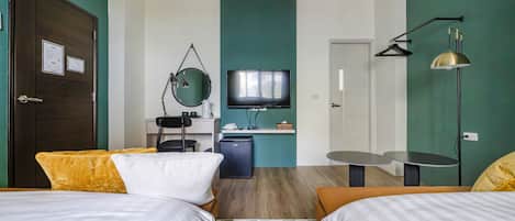 Una habitación de hotel con dos camas, un escritorio con computadora, televisión y un refrigerador pequeño.