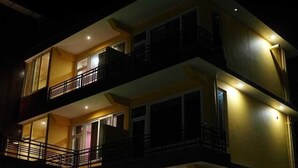 Un edificio de varios pisos con balcones, ventanas amplias y un coche estacionado al frente.