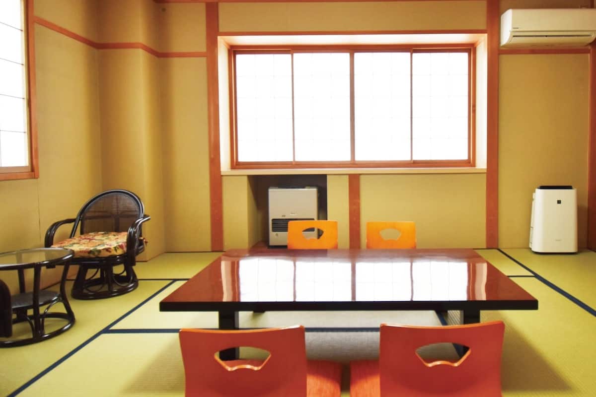 A tatami mat room with a low table, two orange cushions, a television, a refrigerator, and a heater.