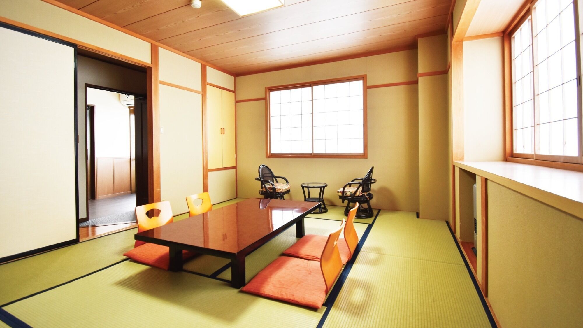 Una habitación con esteras de tatami, una mesa baja, sillas y un ventanal.