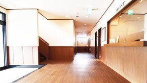 Ein Hotel-Empfangsbereich mit einem Holzbüro, einer linken Treppe und einem Korridor zu weiteren Zimmern.