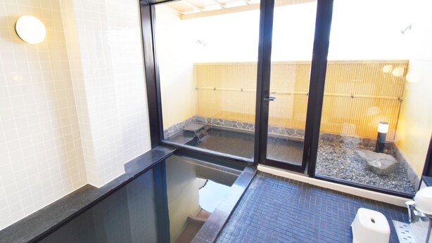 Ein Badezimmer mit Glastrennwand, Fliesenwand, einem Becken aus Stein und einem Bambuszaun, der durch das Glas sichtbar ist.
