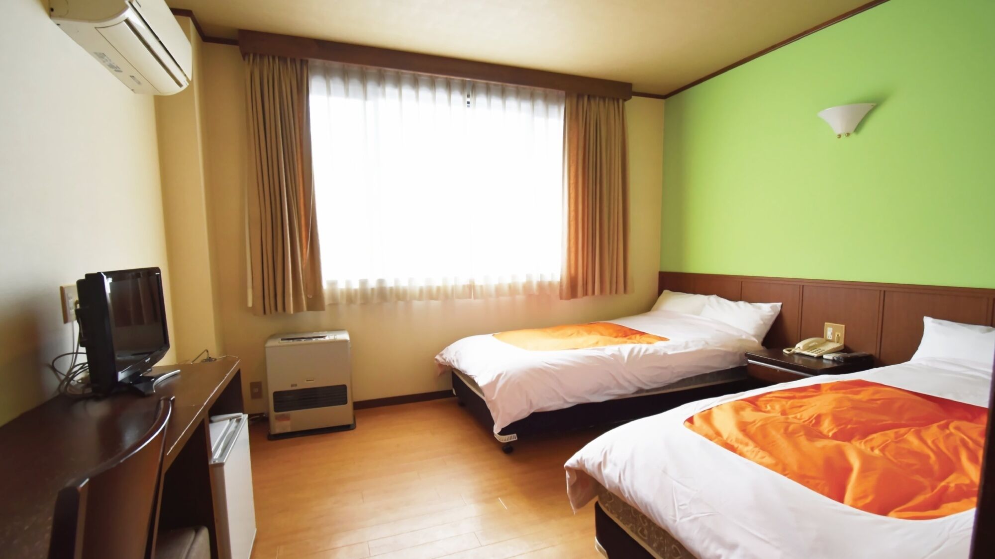 Habitación de hotel con dos camas, un escritorio, una silla, aire acondicionado, una ventana con cortinas y una pared verde.