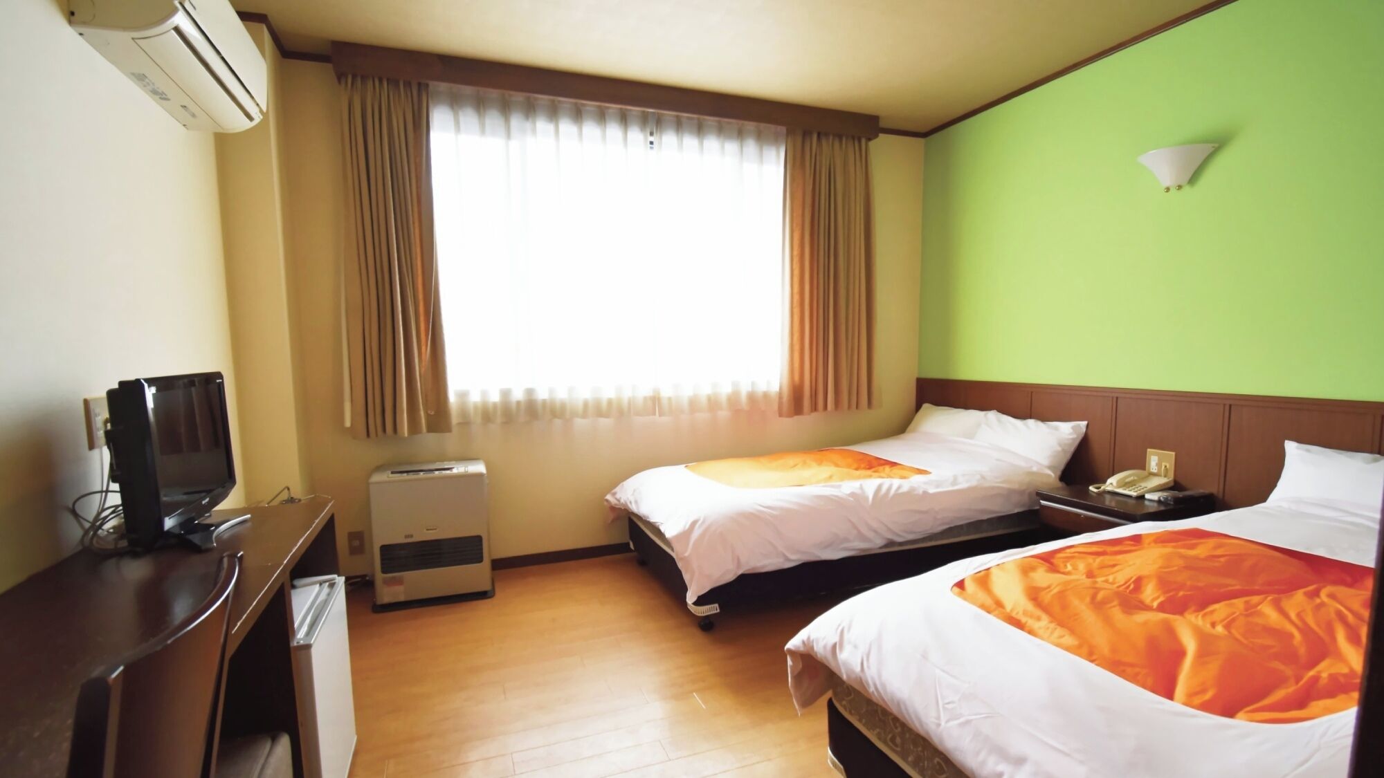 Habitación de hotel con dos camas, un escritorio, aire acondicionado, una ventana con cortinas y una pared verde.
