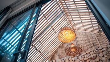 A room with a large window, bamboo slats, a stone wall, and a hanging light fixture.