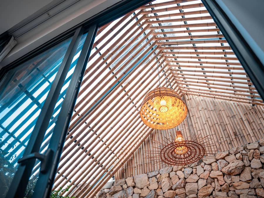 A room with a large window, bamboo slats, a stone wall, and a hanging light fixture.