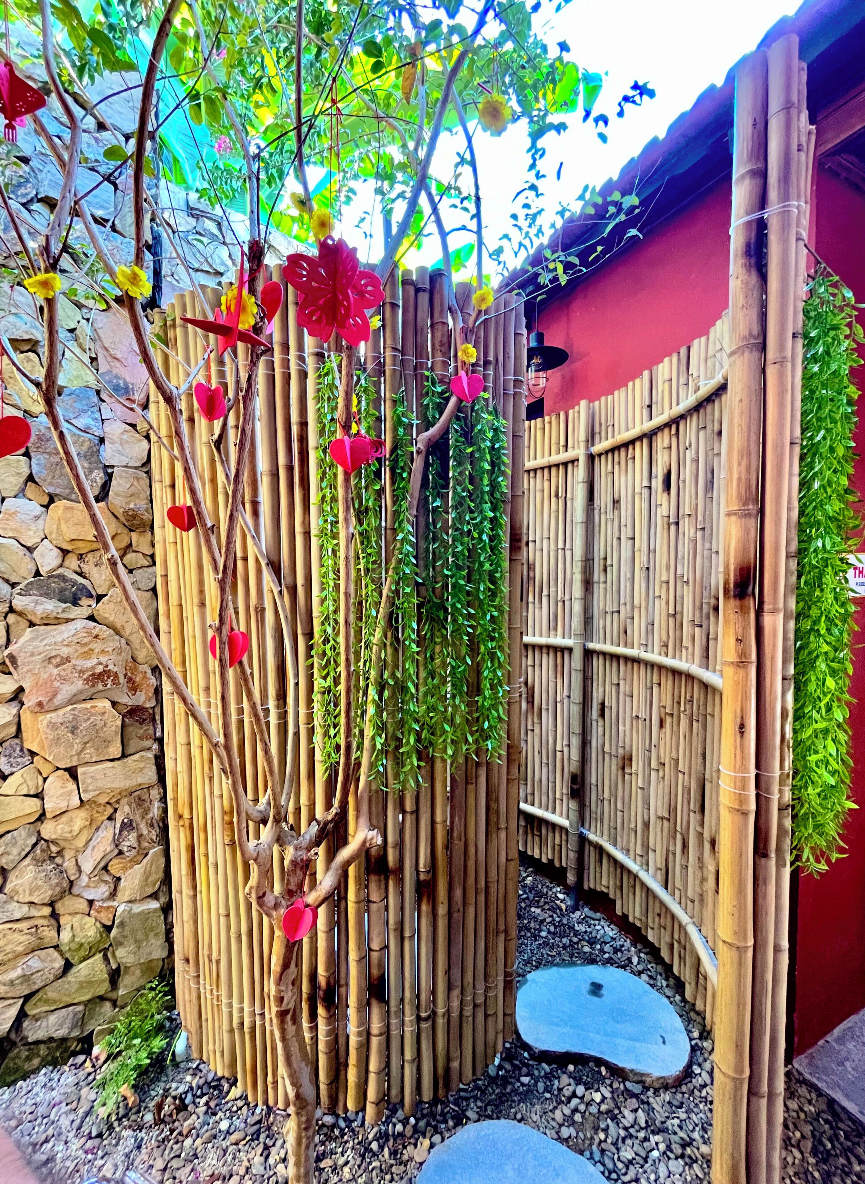 Una valla de bambú, un muro de piedra y una pequeña piscina.