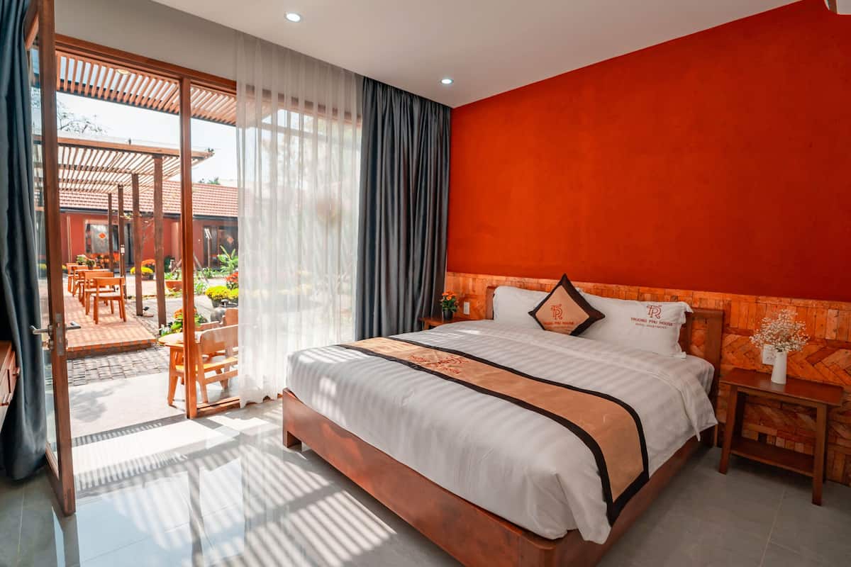A spacious bedroom with a large bed, a sliding glass door leading to an outdoor patio, and a red accent wall.