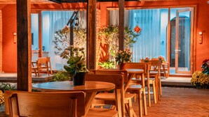 A covered outdoor seating area with wooden tables and chairs, potted plants, and a view of the interior through glass doors. - TRUONG PHU HOUSE (Hue)