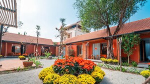 A courtyard with a central flower arrangement, a building with red-tiled roofs, and a tree. - TRUONG PHU HOUSE (Hue)