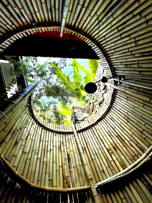 A circular bamboo structure with a central opening, a metal railing, and a view of greenery outside. - TRUONG PHU HOUSE (Hue)