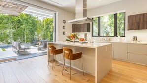 A modern kitchen with a large island, bar stools, and a view of a garden.