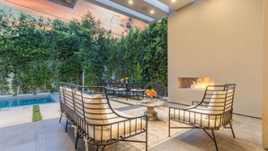 An outdoor patio with a pool, two lounge chairs, a table, and a fire feature.