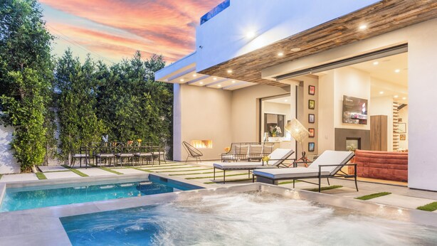 A modern outdoor pool area with lounge chairs, a hot tub, and a patio with seating.