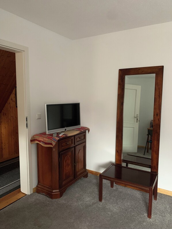 A room with a wooden cabinet, a television, and a mirror on the wall.