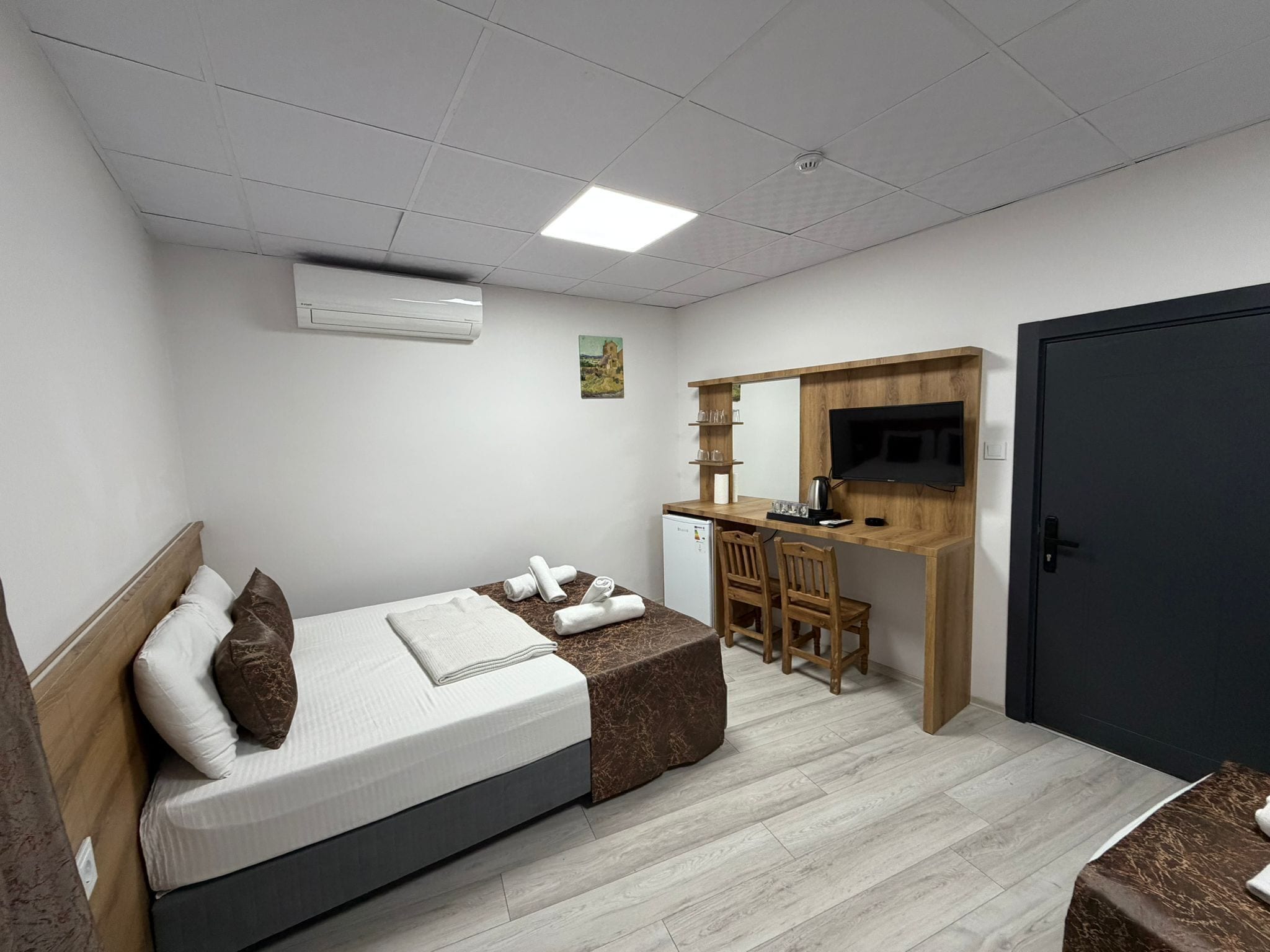 Un dormitorio con cama, escritorio, silla, televisor y puerta.