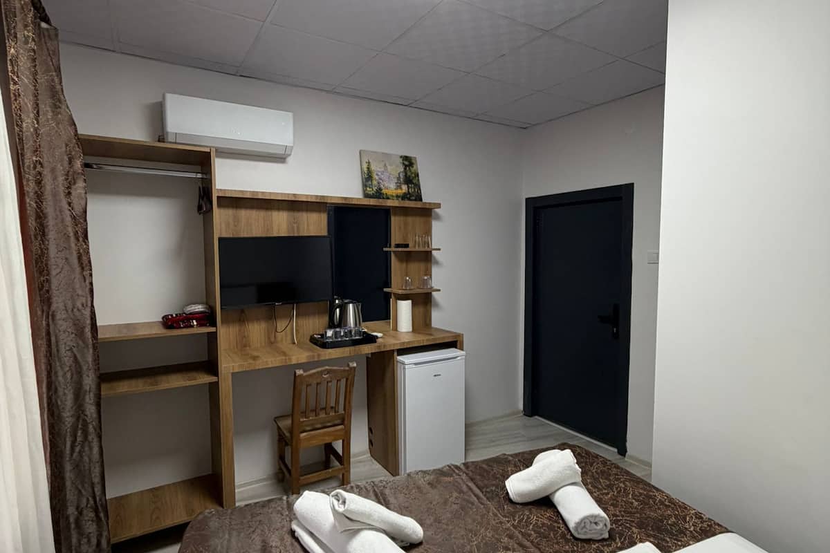 Ein Hotelzimmer mit Bett, Schreibtisch, Stuhl, kleinem Kühlschrank und Ablagefach für Toilettenartikel.