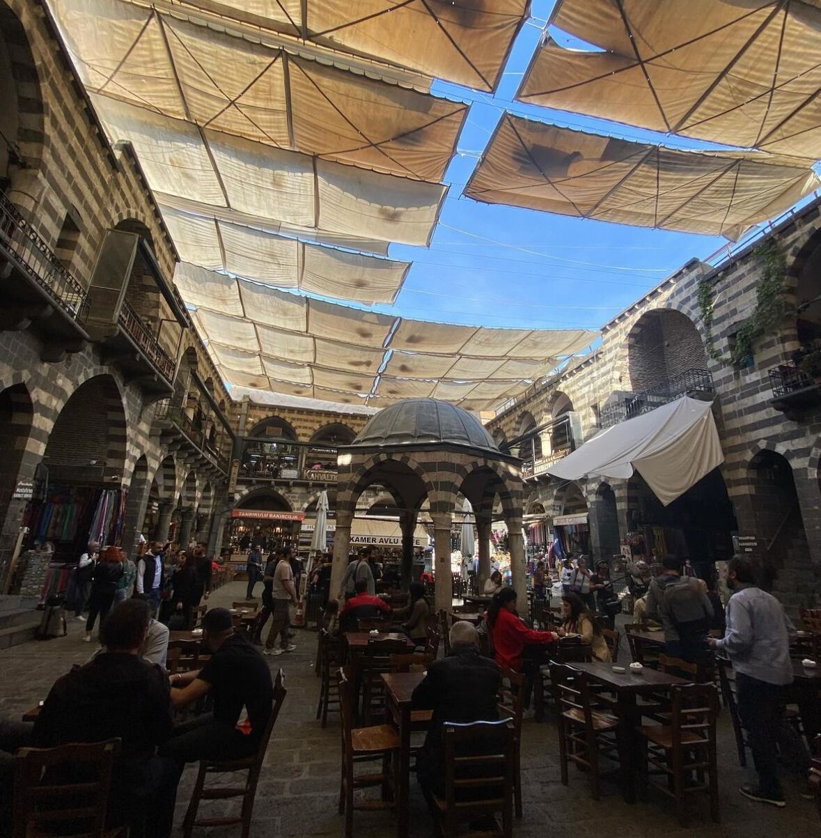 Un marché couvert avec des arcades en pierre, des étals et des clients qui font leurs courses.