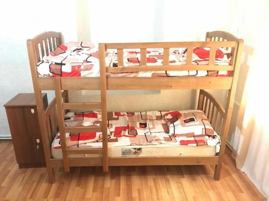 A bunk bed with a patterned bedspread, a wooden headboard, and a small wooden cabinet beside it.
