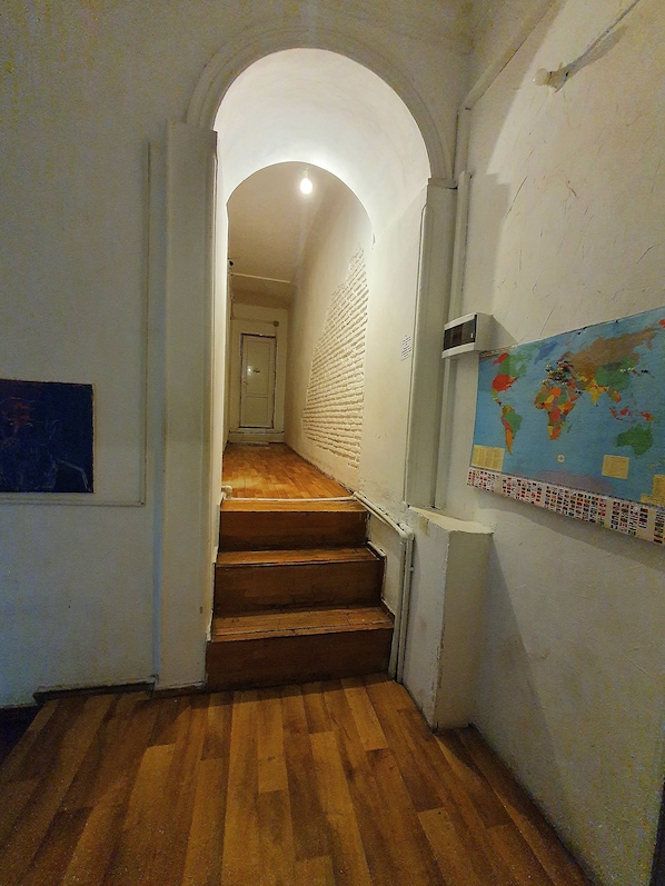 A narrow hallway with wooden flooring and a white brick wall. A map is displayed on the right wall. - Machabelli Hostel (Tbilisi)