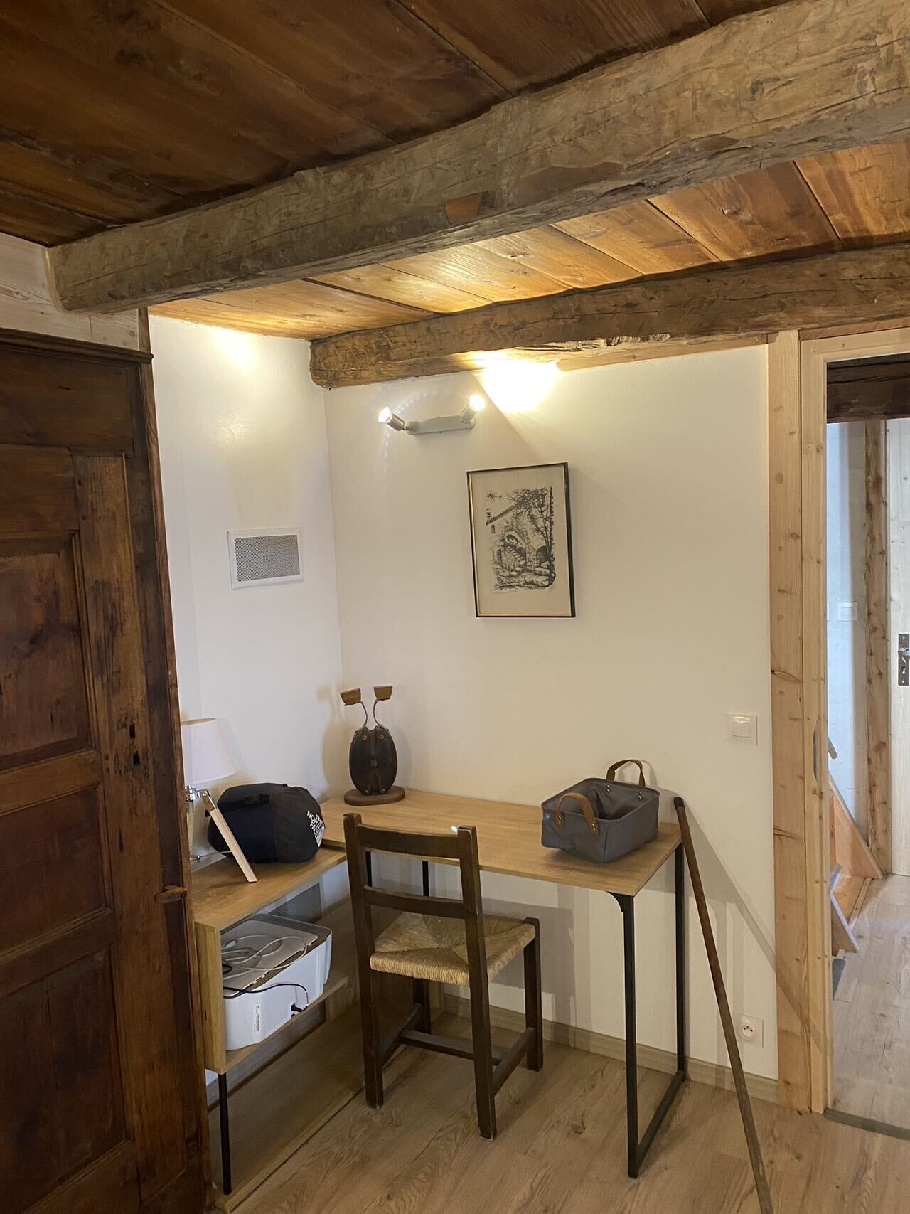Una habitación rústica con techo de madera, un escritorio con una silla, una lámpara y un cuadro en la pared.