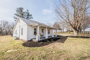 A single-story white house with a porch, a small garden, and a tree in the background. - Mammoth Cave Getaway (Cave City)