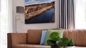 A living room with a brown leather sofa, a wall-mounted lamp, a framed landscape painting, and a potted plant on a white table. - Luxury Home by De Alde Feanen Reserve (Earnewald)