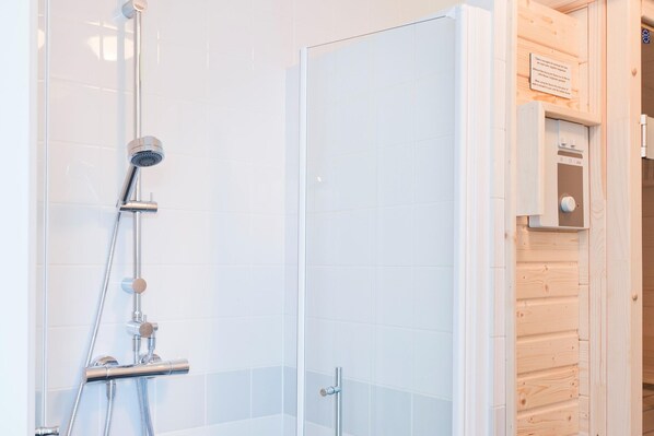 A shower with a glass door, a wooden panel wall, and a control panel on the right.