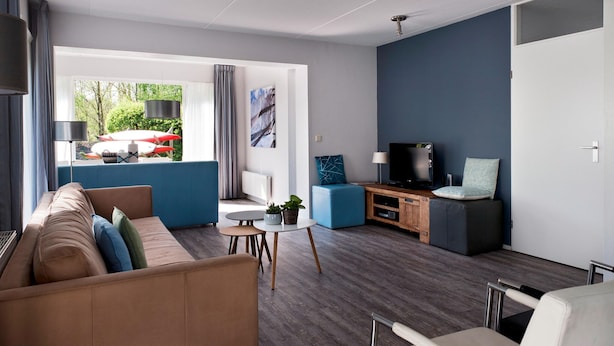 A modern living room with a sofa, a coffee table, a TV, and a dining area with a table and chairs. - Luxury Home by De Alde Feanen Reserve (Earnewald)