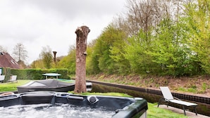 A hot tub in a garden with a bench and a tree.