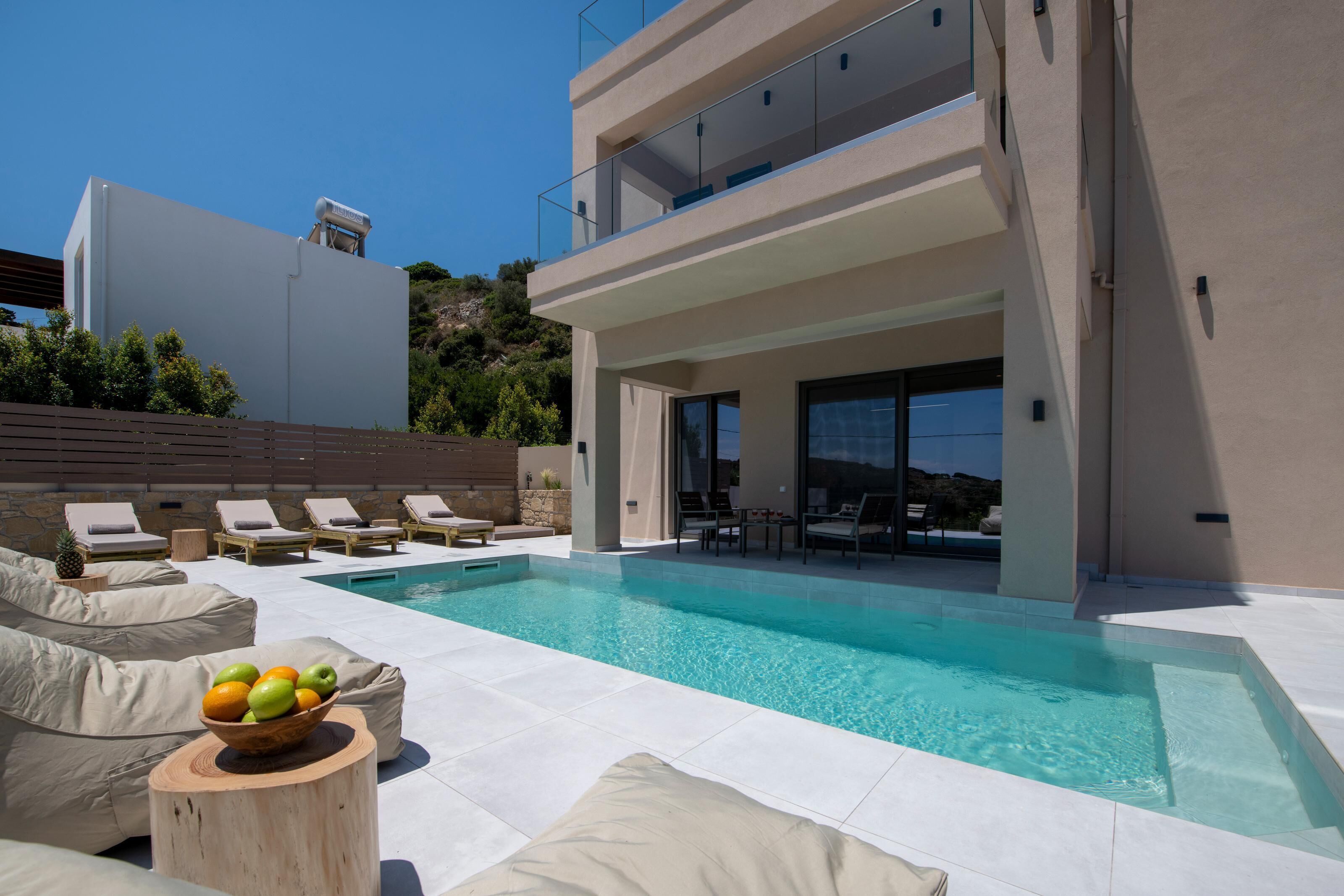 A modern pool area with lounge chairs, a wooden table with fruit, and a clear view of the pool.