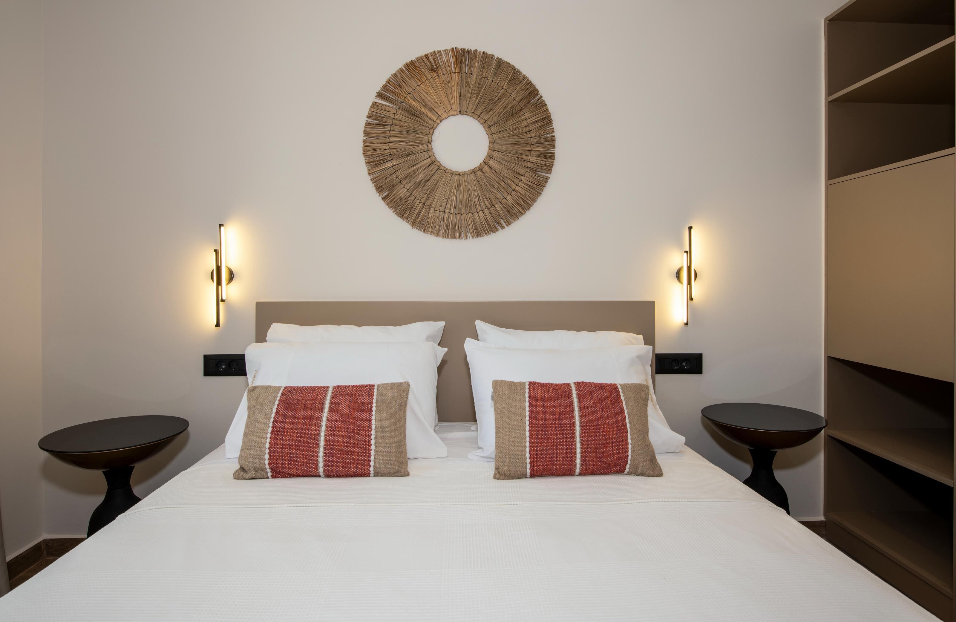 A hotel room with a large bed, two bedside tables, a wall-mounted circular light fixture, and a wardrobe.