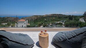 A balcony with a wooden stool and two glasses of red wine, overlooking a coastal landscape with buildings and greenery. - Armour Eclectic Villa (Platanias)