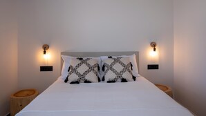 A bedroom with a bed, two wall-mounted light fixtures, and two wooden nightstands. - Armour Eclectic Villa (Platanias)